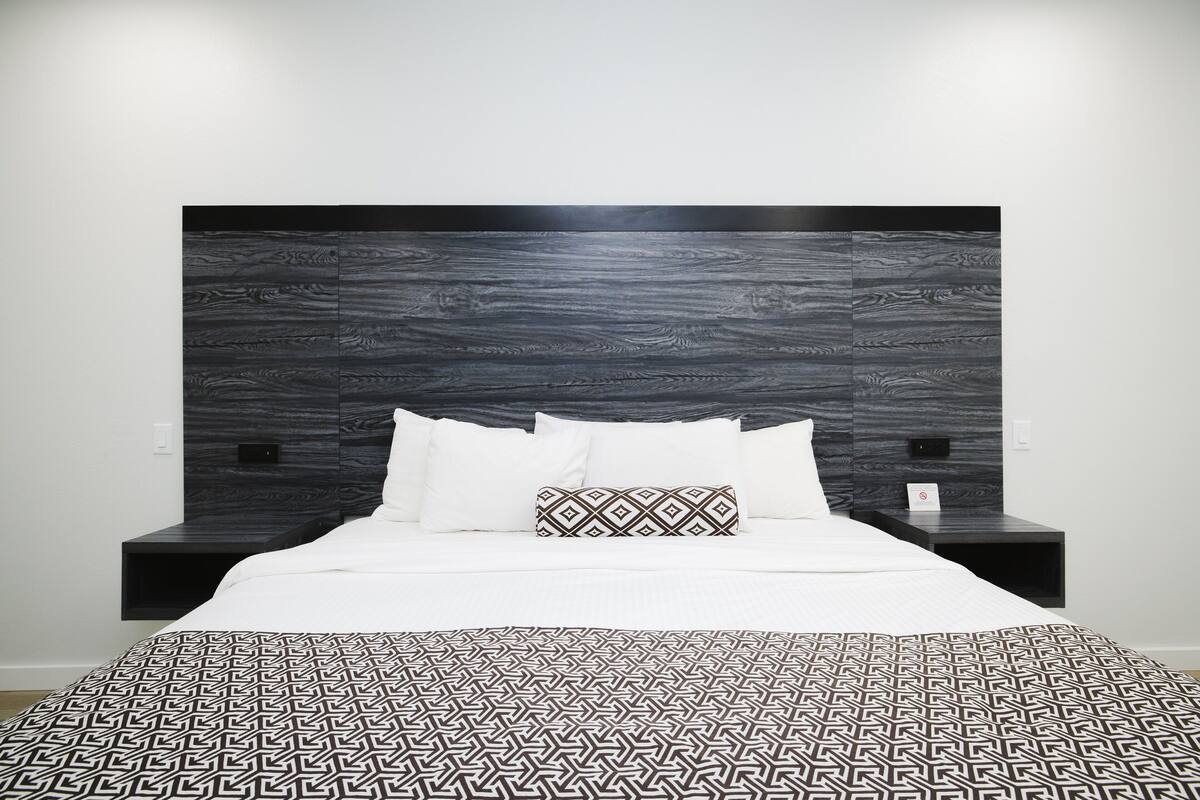 A modern bedroom with a dark wood headboard, white bedding, and a geometric-patterned bedspread.