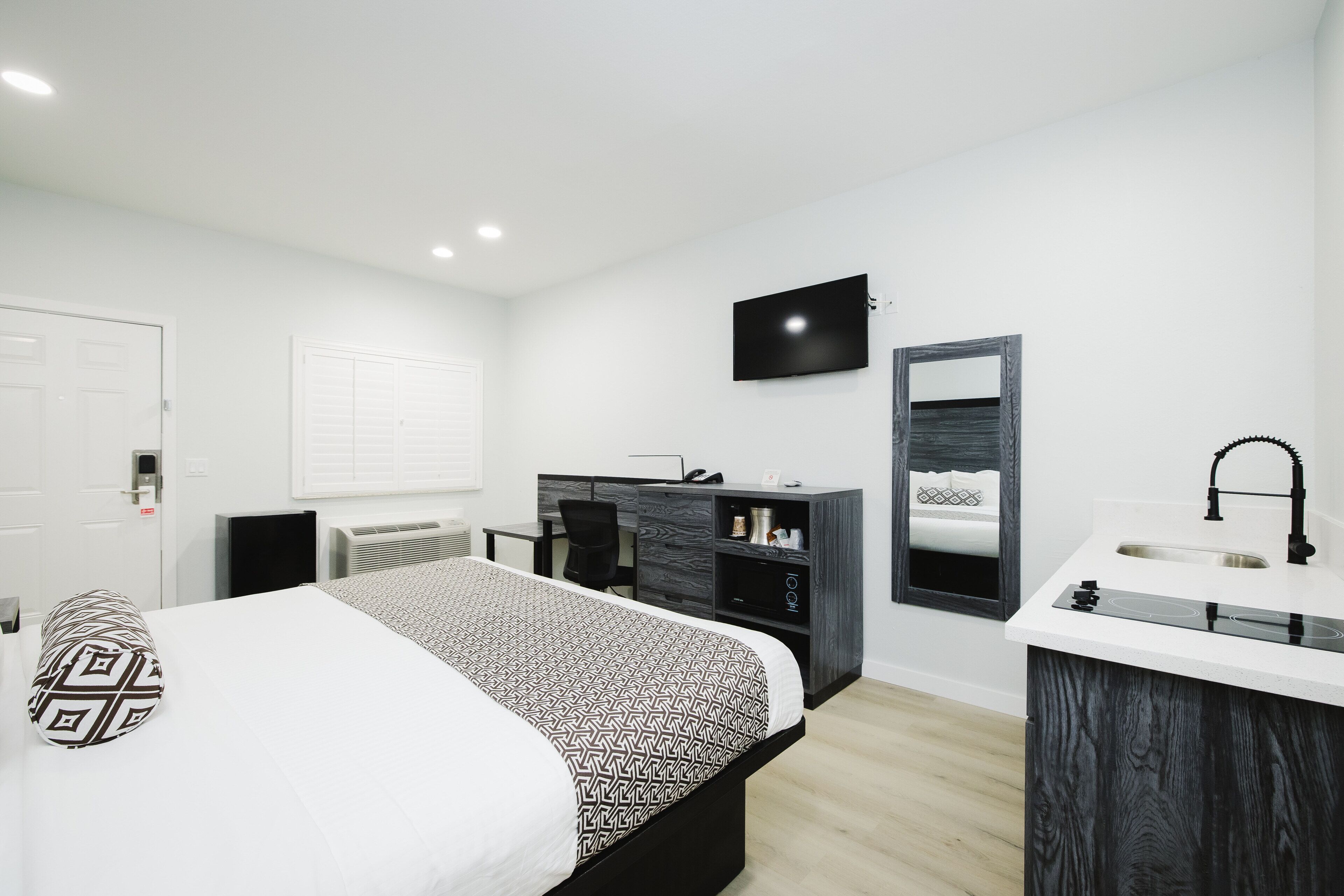Ein modernes Schlafzimmer mit Bett, Schreibtisch, Fernseher, Spiegel und einem Badezimmer mit Waschbecken und Dusche.