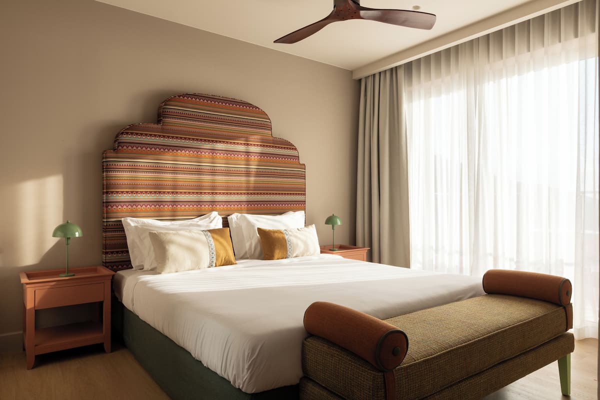Ein Hotelzimmer mit einem großen Bett, einem Deckenventilator, einem Nachttisch mit Lampe und einem Fenster mit Vorhängen.