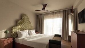 Een hotelkamer met een bed, nachtkastje, kledingkast, televisie en plafondventilator.