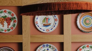 Een eetruimte met een houten wand versierd met kleurrijke borden, een tafel met kaarsen en rieten stoelen.