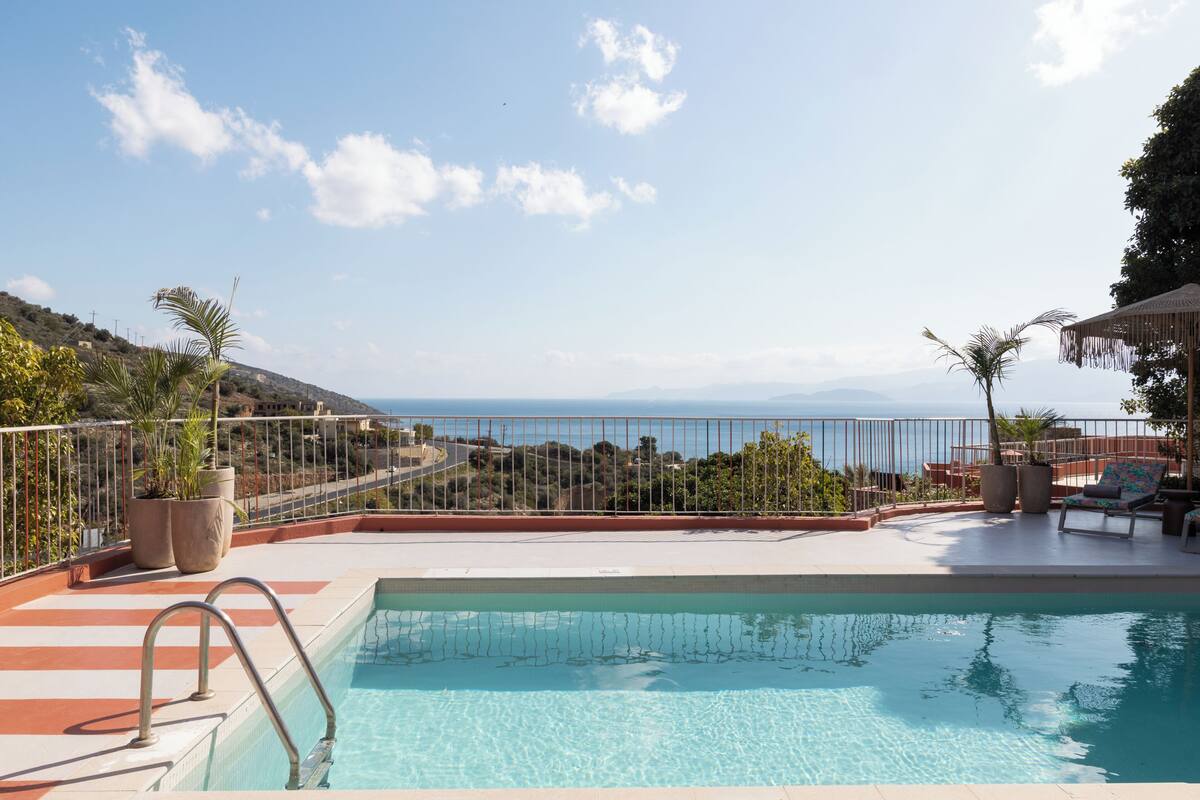 Ein Pool mit Meerblick, eine umzäunte Terrassenfläche und Liegestühle.