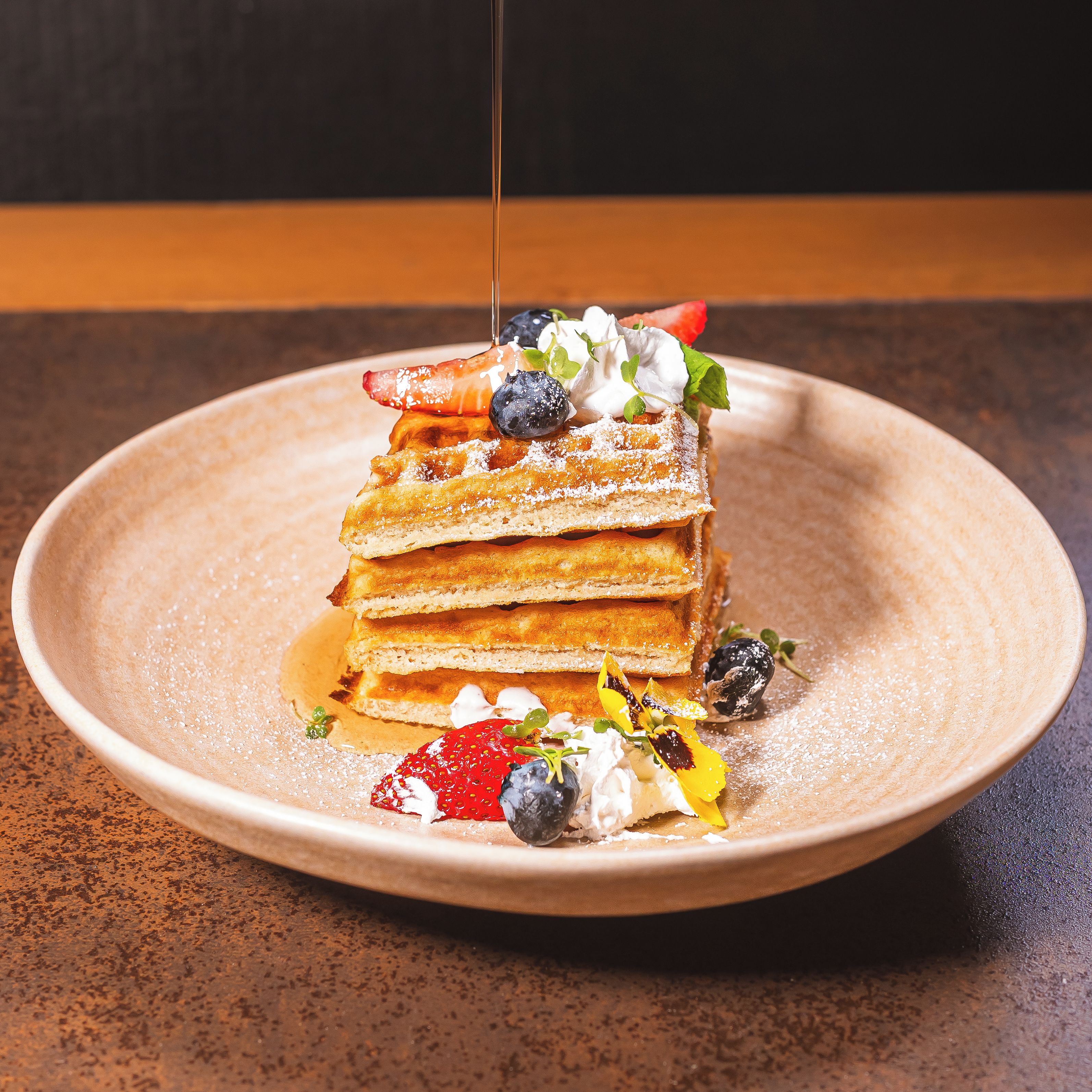 Une pile de crêpes nappées de sirop et garnies de fruits, le tout présenté sur une assiette.