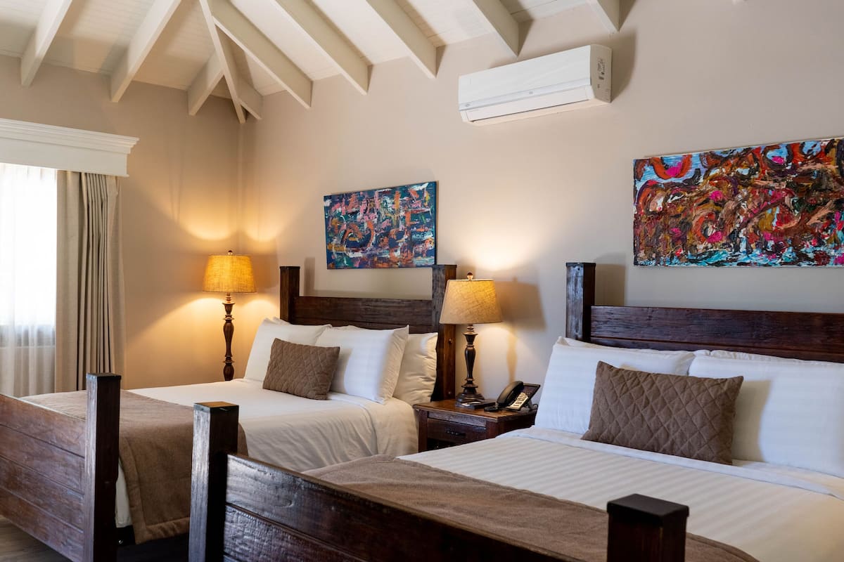 A hotel room with two beds, a ceiling fan, and artwork on the walls.