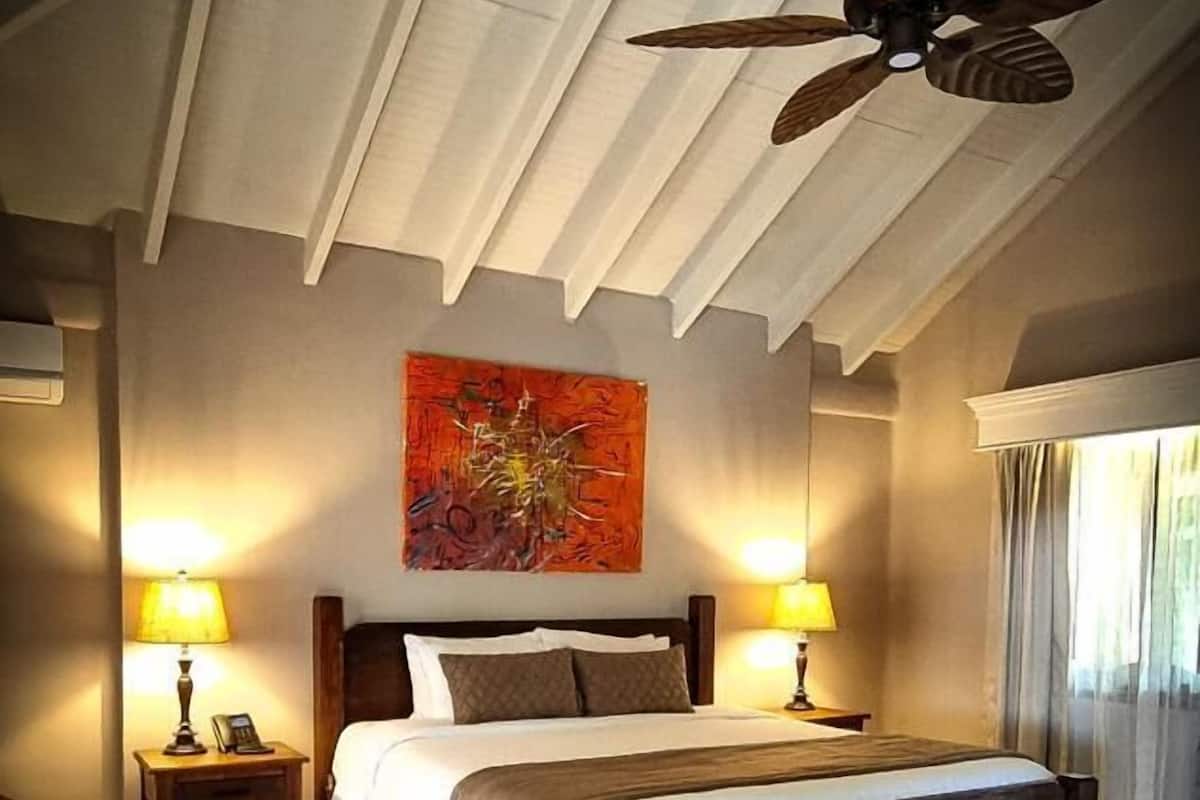 A bedroom with a large bed, two bedside tables with lamps, a ceiling fan, and a large abstract painting on the wall.