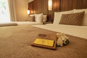 Un lit bien fait, avec une tête de lit en bois, une table de chevet avec une lampe et une carte de bienvenue posée sur le lit.