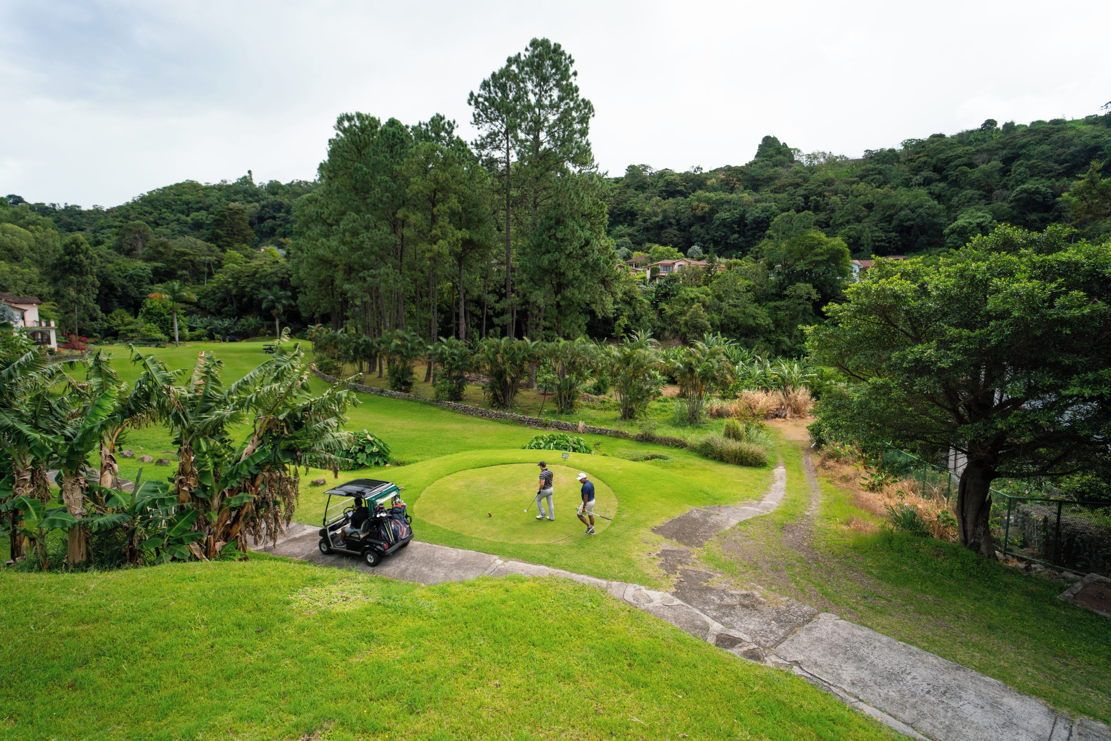 Un campo de golf con un club de campo, un carrito de golf y un jugador en el green.