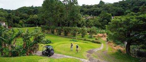Un campo de golf con un club de campo, un carrito de golf y un jugador en el green.
