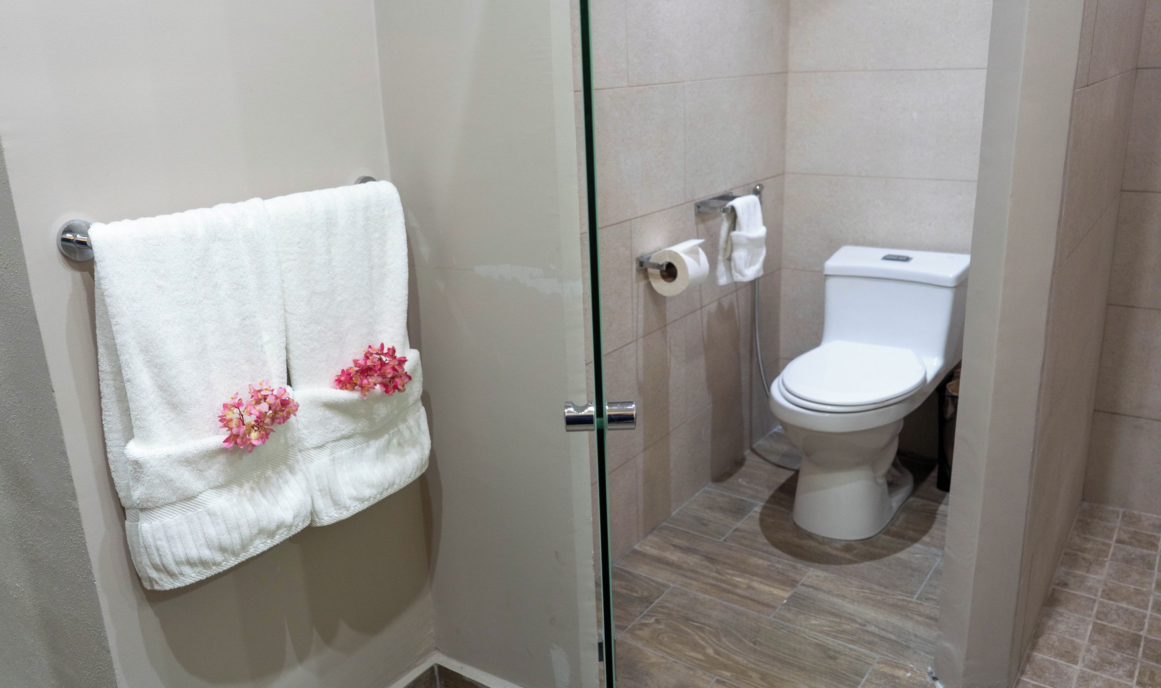 Un baño con mampara de vidrio, inodoro blanco y toalla con motivos florales rosas.