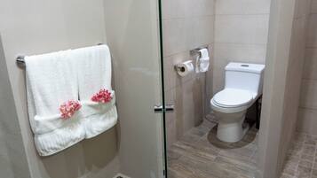 Un baño con mampara de vidrio, inodoro blanco y toalla con motivos florales rosas.
