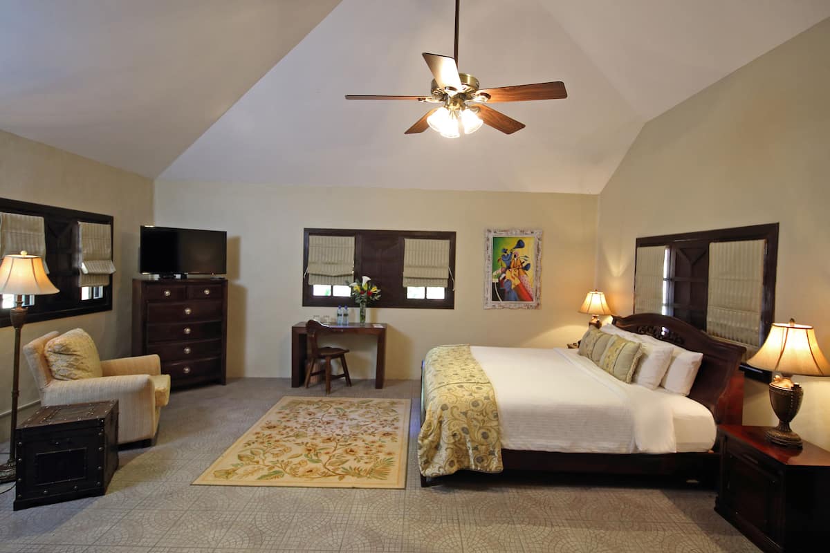 A hotel room with a bed, desk, chair, dresser, and a ceiling fan.