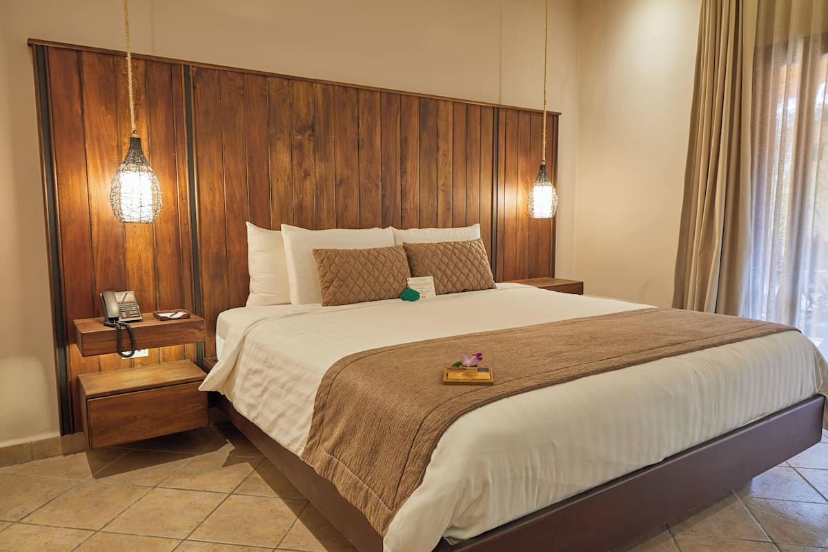 A hotel room with a wooden headboard, a bed with white linens, a nightstand with a phone, and a bedside table with a lamp.