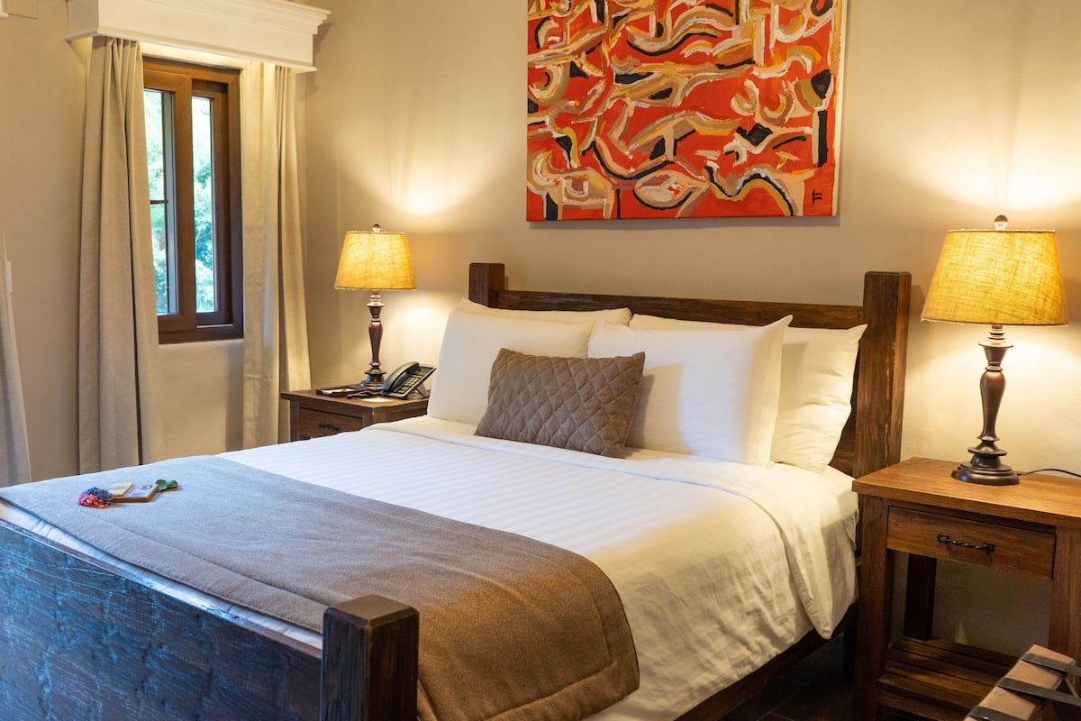A neatly made bed with white linens, a quilted pillow, and a bedside lamp on a wooden nightstand.