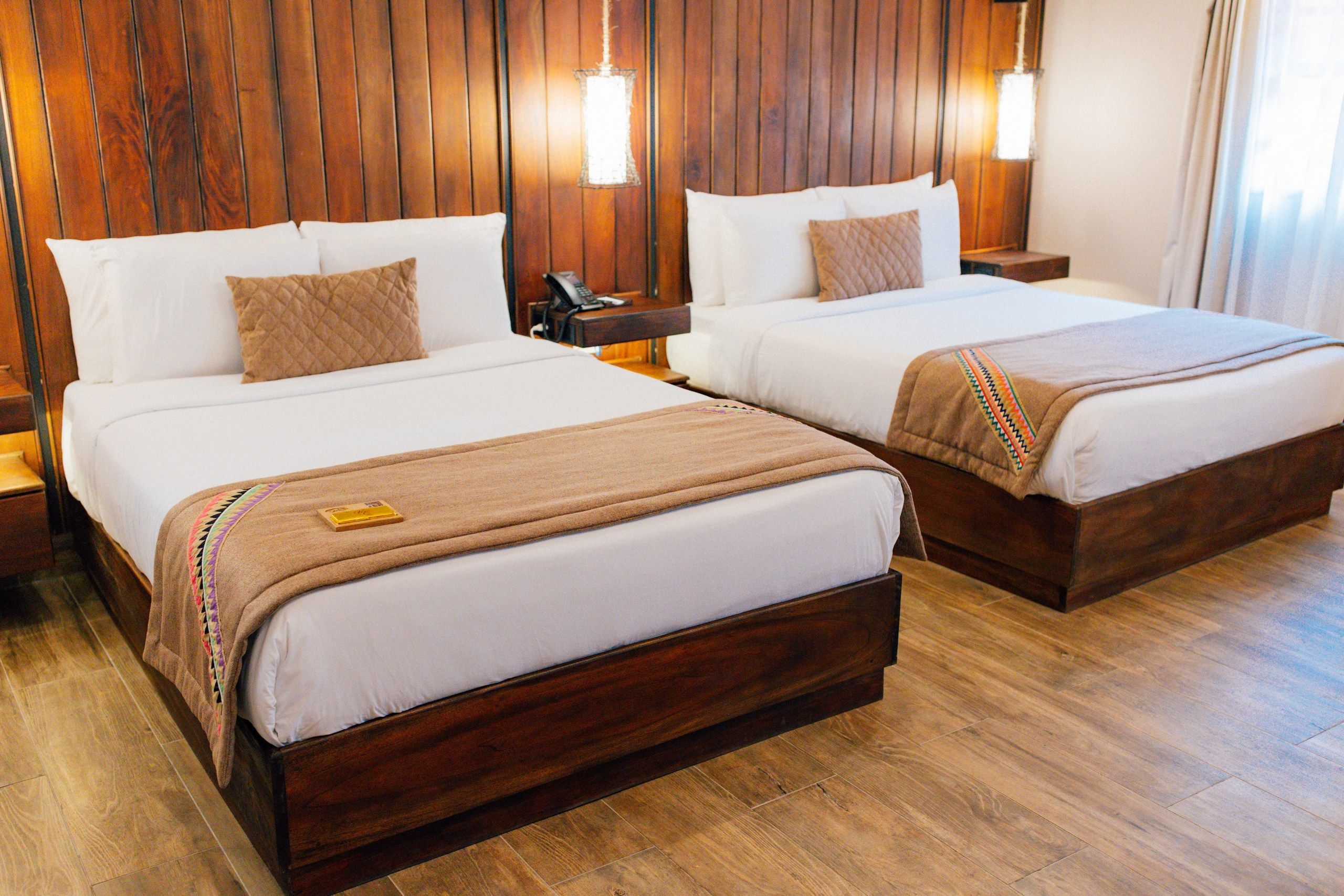 Habitación de hotel con dos camas, cabeceros de madera, mesitas de noche y un teléfono.
