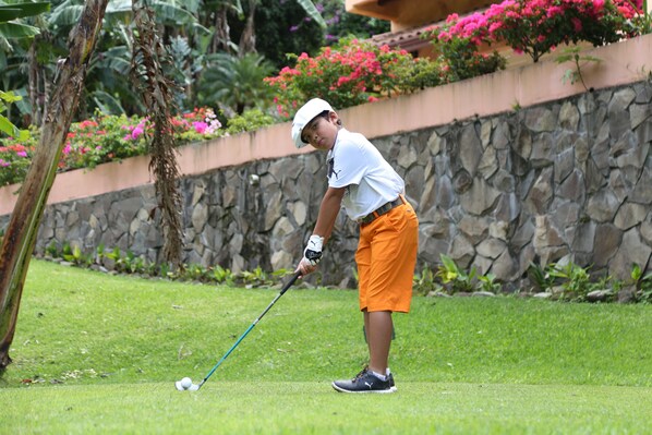 A person playing golf on a well-maintained grass course with a stone wall and colorful flowers in the background.