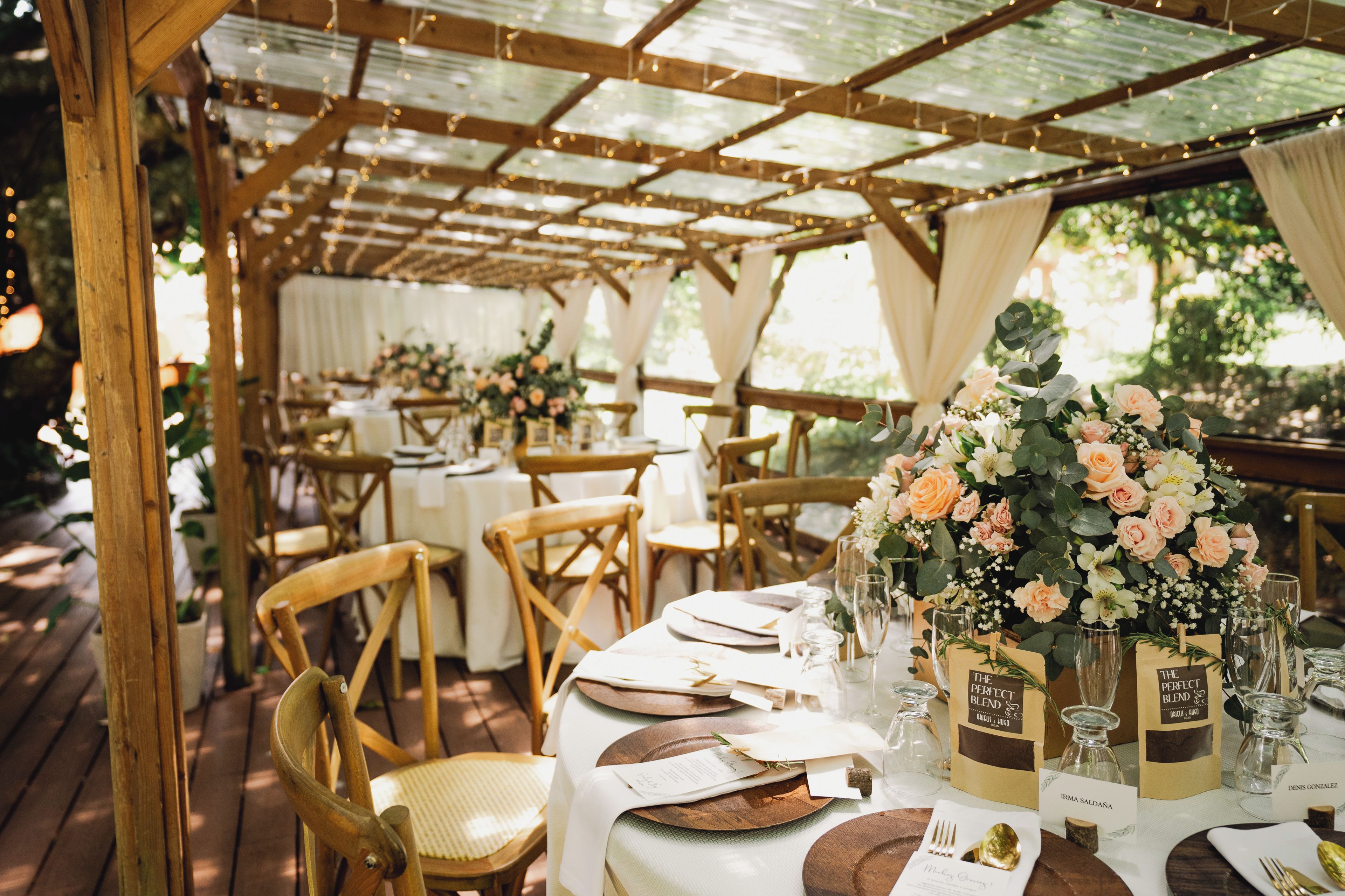 An outdoor dining area with wooden tables and chairs, covered by a wooden pergola.