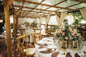 Un área de comedor al aire libre con mesas y sillas de madera, cubierta por una pérgola de madera.