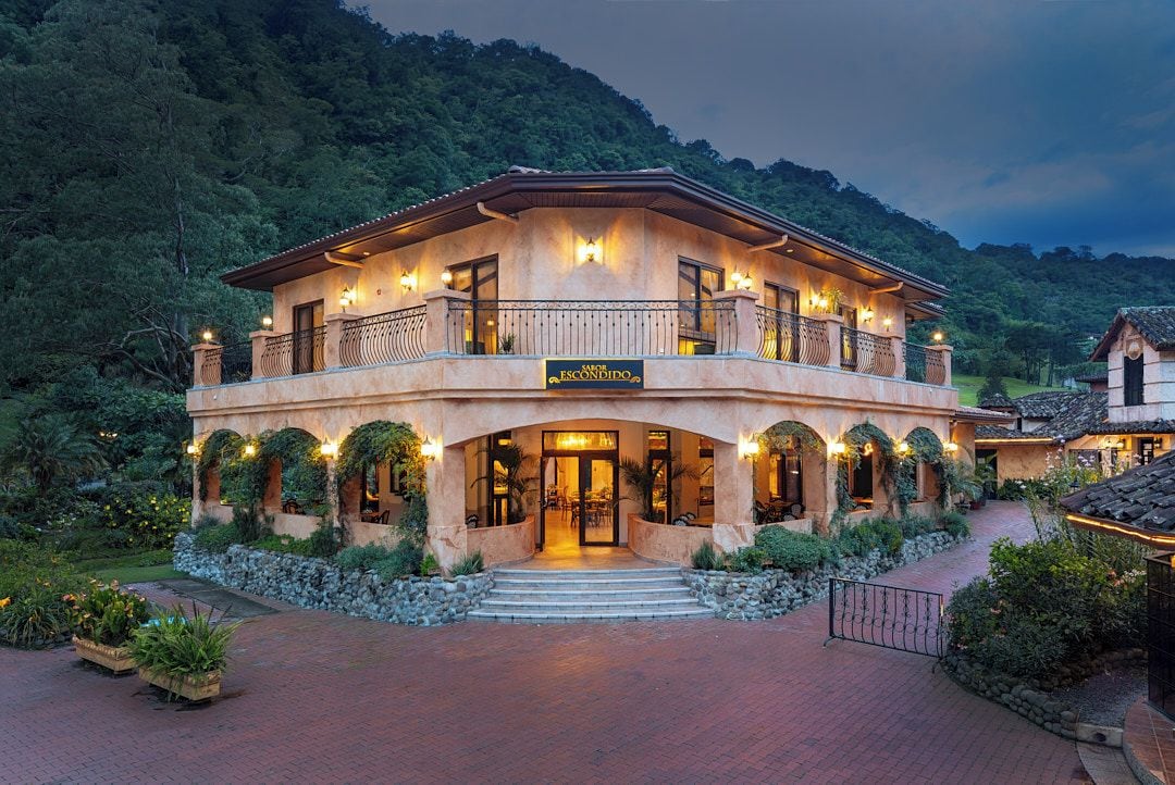 A two-story building with a balcony, a sign reading 'MASOR ESCONDIDO,' and a stone pathway leading to the entrance.