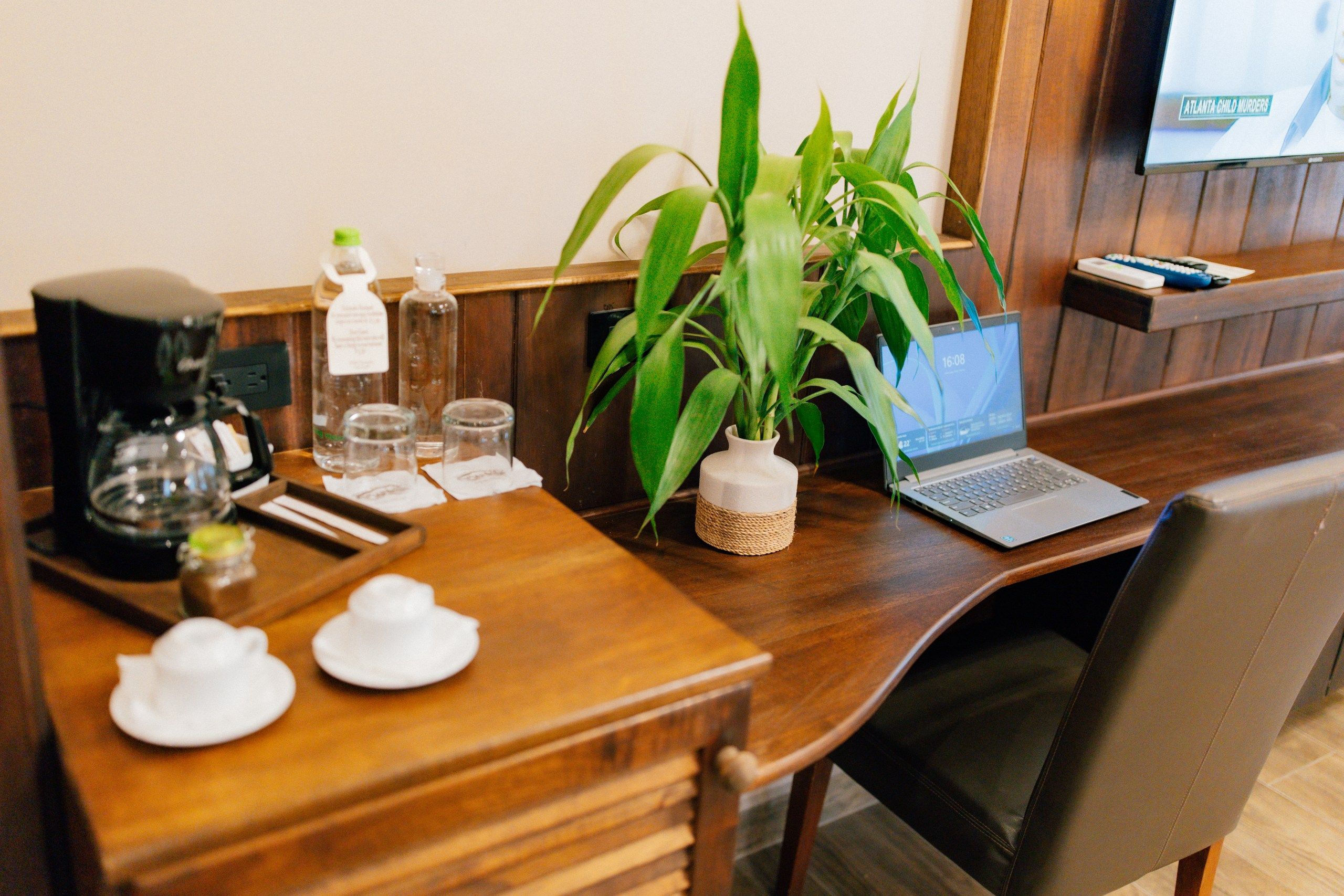 A wooden desk with a laptop, a coffee maker, and a potted plant.