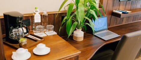 A wooden desk with a laptop, a coffee maker, and a potted plant.