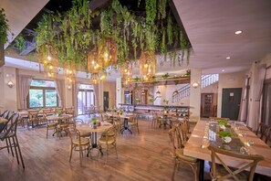 Un restaurante espacioso con techos altos, plantas colgantes y diferentes tipos de mesas y sillas, incluyendo mesas redondas.