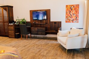 Un salon avec un téléviseur à écran plat fixé à un mur en bois, un canapé blanc, un bureau avec une chaise, une plante et une machine à café.