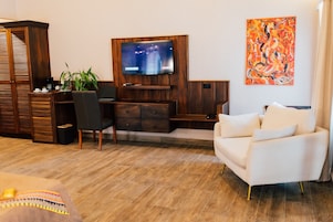 Un salón con una televisión de pantalla plana montada en una pared de madera, un sofá blanco, un escritorio con una silla, una planta y una cafetera.