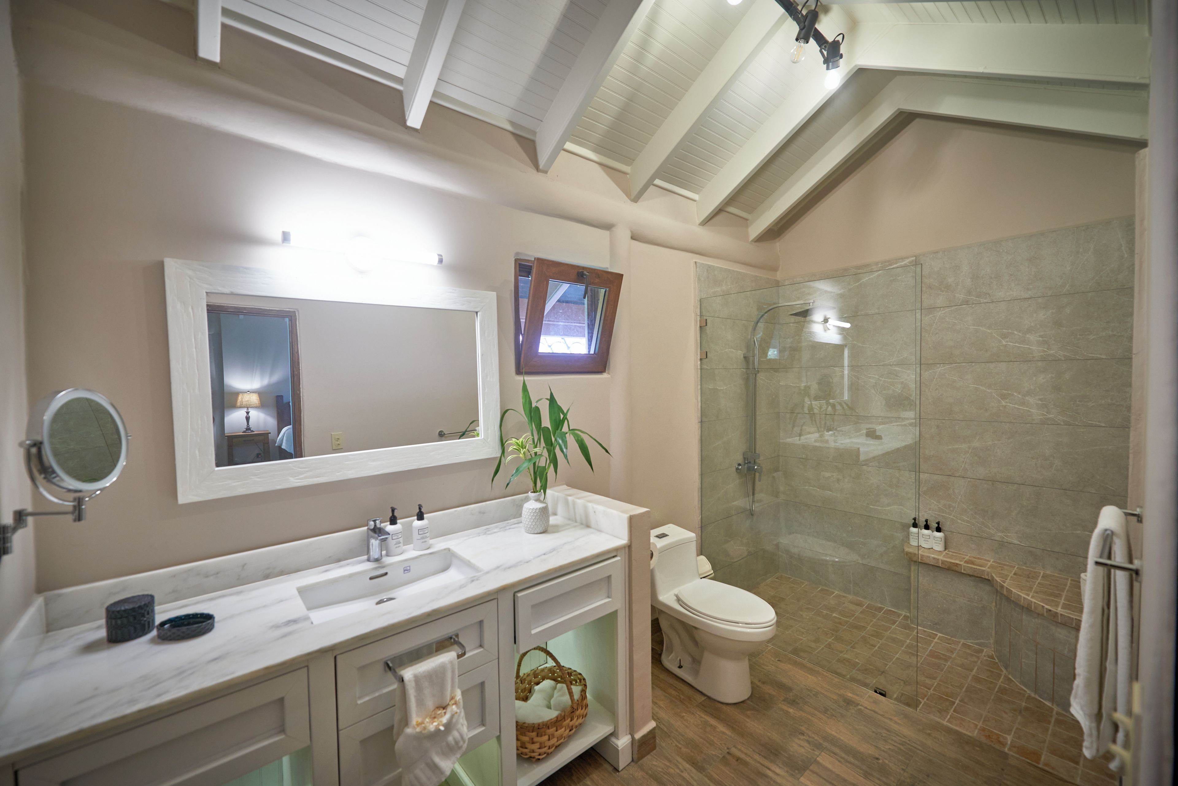 A bathroom with a marble vanity, a toilet, a glass-enclosed shower, and a small window.