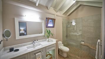 A bathroom with a marble vanity, a toilet, a glass-enclosed shower, and a small window.