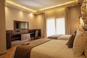 Habitación de hotel con cama, escritorio, televisión y ventana con cortinas.