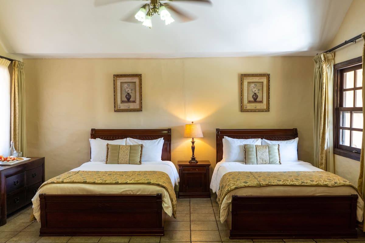 A double room with two beds, a nightstand with a lamp, a dresser, and a window with curtains.
