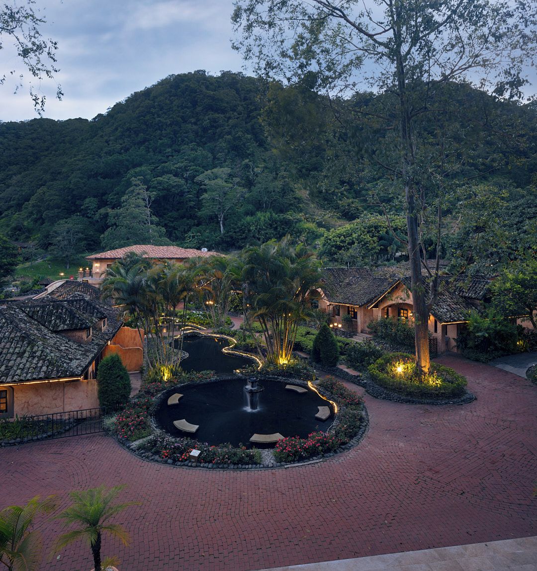 Un resort con diversi edifici, un elemento d'acqua centrale e montagne sullo sfondo.
