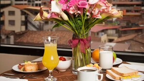 A breakfast table with a vase of flowers, a glass of orange juice, a cup of coffee, and a plate with toast and eggs. - HOTEL MABEY CUSCO (Cusco)