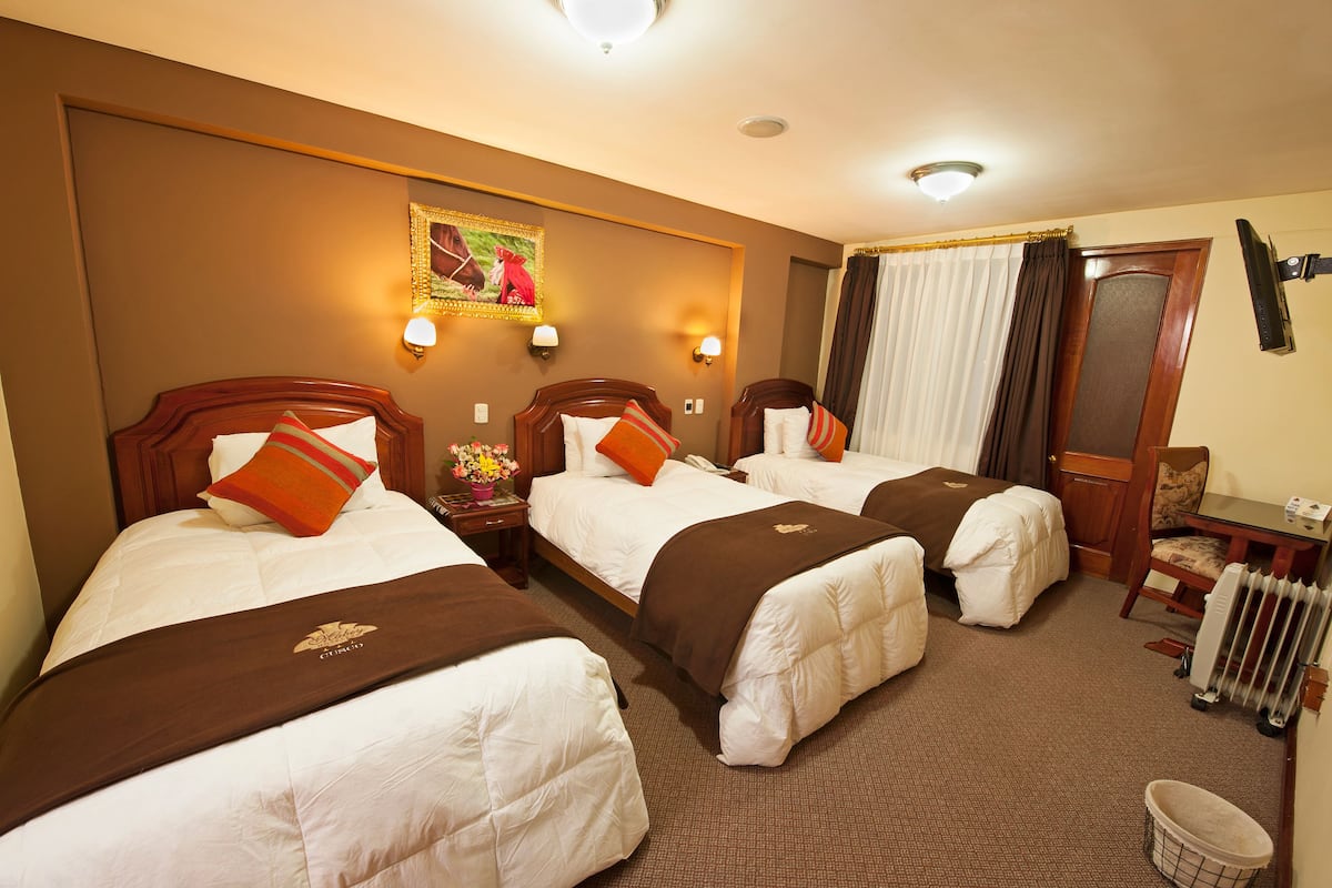 A hotel room with three beds, a small table, a chair, a radiator, and a painting on the wall.
