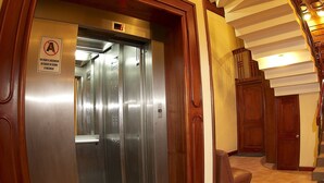 An elevator with a sign indicating it is not in use, a welcome mat, and a staircase with wooden railings. - HOTEL MABEY CUSCO (Cusco)