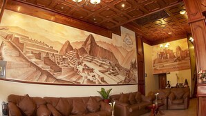 A lobby with a large mural of a mountainous landscape, a brown leather sofa, and a wooden ceiling with recessed lighting. - HOTEL MABEY CUSCO (Cusco)