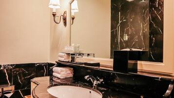 A bathroom with a round sink, black marble countertops, a large mirror, and wall-mounted lights.