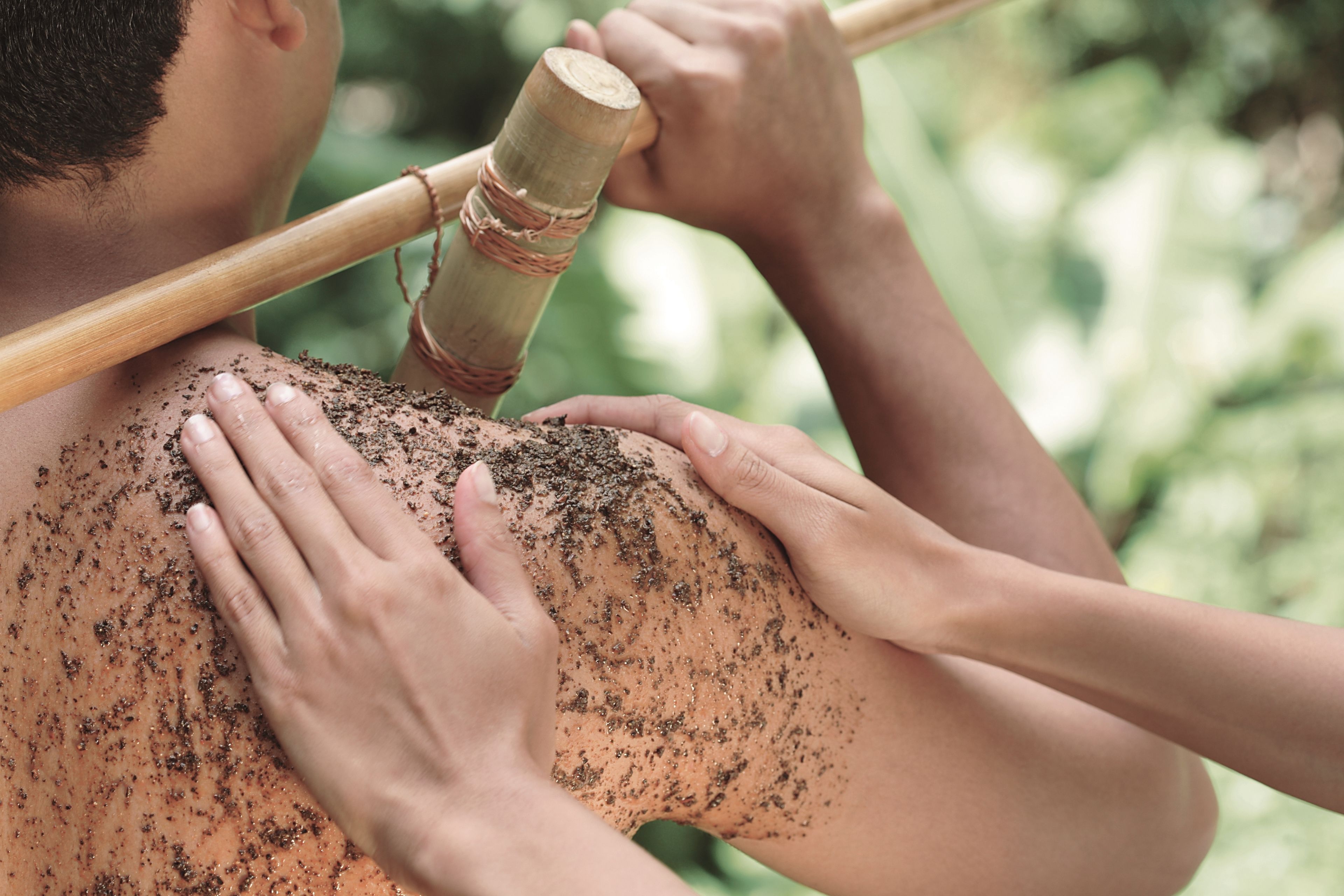 A person receiving a massage with a wooden tool on their shoulder.