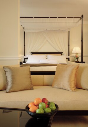 A hotel room with a bed, a nightstand with a lamp, a sofa with cushions, and a table with a fruit bowl.