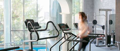 A gym with treadmills, weight machines, and a large window with a view of trees.