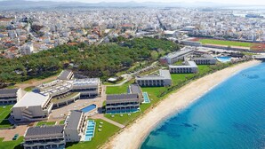 Vue aérienne d’un hôtel situé sur la côte, composé de plusieurs bâtiments, avec une plage et une mer d’un bleu limpide.