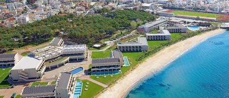 An aerial view of a coastal hotel with multiple buildings, a beach, and a clear blue sea.