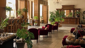 Un hall d’entrée spacieux avec des boiseries, un bar, de nombreux espaces pour s’asseoir, notamment des canapés et des fauteuils en cuir, et une variété de plantes en pot.
