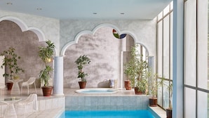Un espace piscine avec une piscine à l’eau d’un bleu limpide, des plantes en pot et des chaises blanches.