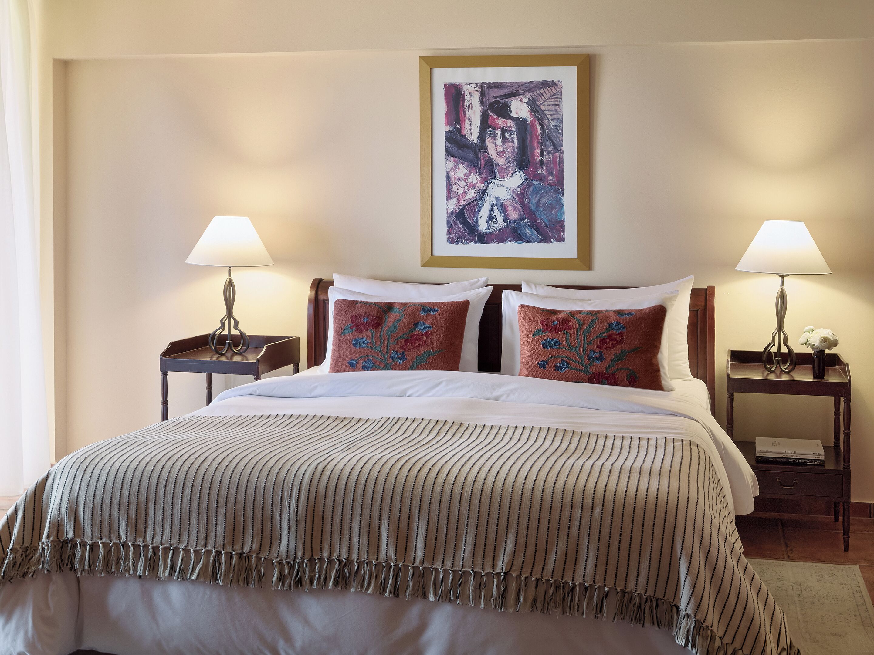 A neatly made bed with a striped blanket and two pillows, flanked by bedside tables with lamps and a framed artwork above.