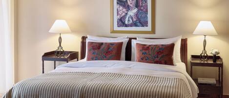 A neatly made bed with a striped blanket and two pillows, flanked by bedside tables with lamps and a framed artwork above.