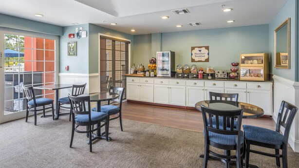 A breakfast bar with seating, a refrigerator stocked with food, and a sign indicating breakfast service. - MainStay Suites Port Saint Joe South (Port St. Joe)