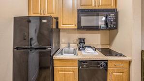 A compact kitchen with wooden cabinets, a stainless steel refrigerator, a microwave, a dishwasher, and a coffee maker. - MainStay Suites Port Saint Joe South (Port St. Joe)