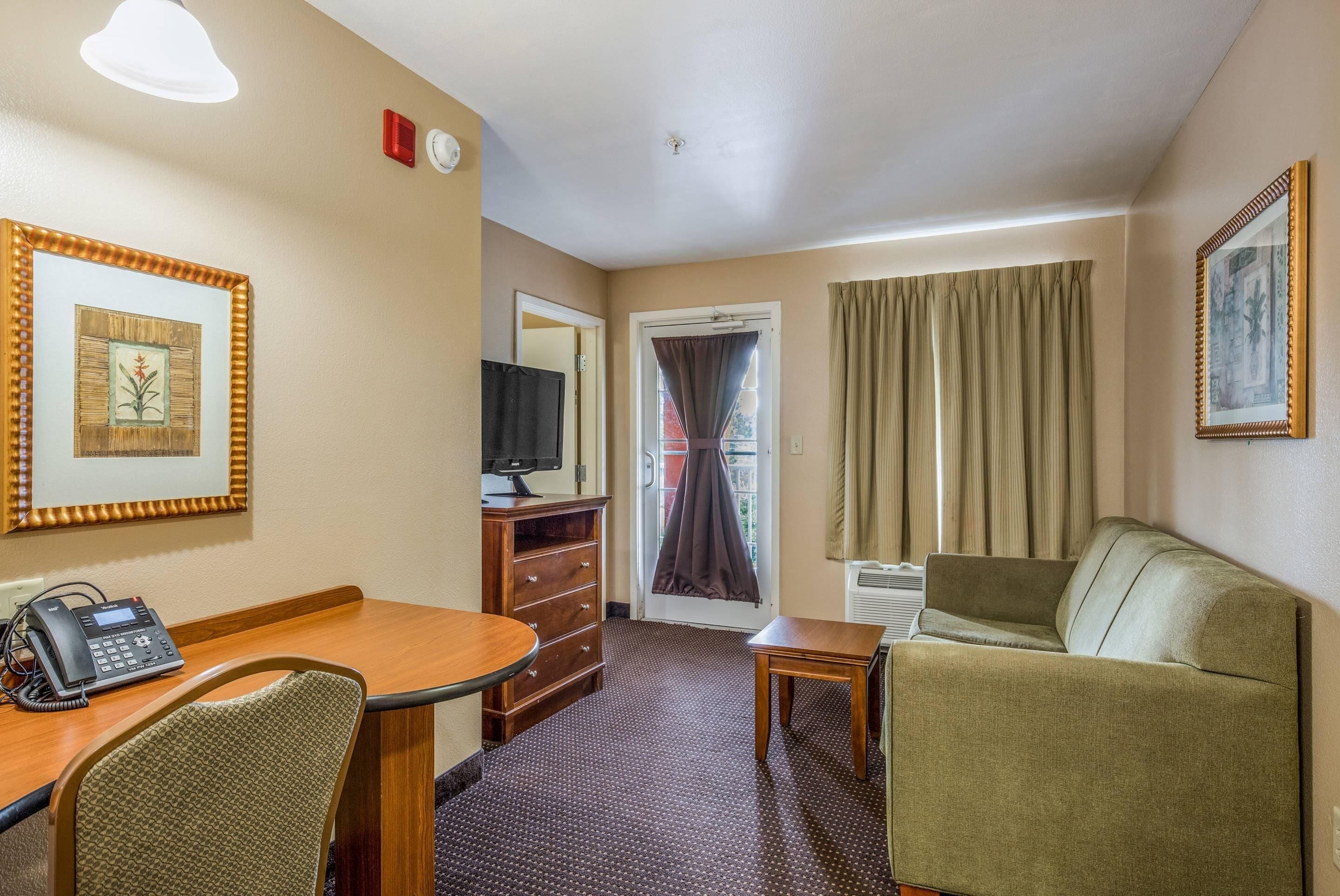 Une chambre d’hôtel avec un bureau en bois, un téléphone, une télévision, un canapé et une porte avec des rideaux.
