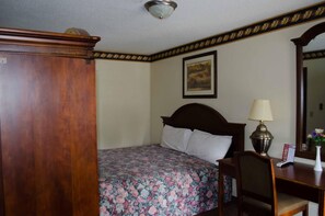 A hotel room with a bed, a desk, a chair, a lamp, a framed picture on the wall, and a mirror. - Delta Motel (Bay City)